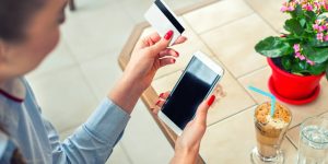 Mulher com um celular e um cartão de crédito em mãos