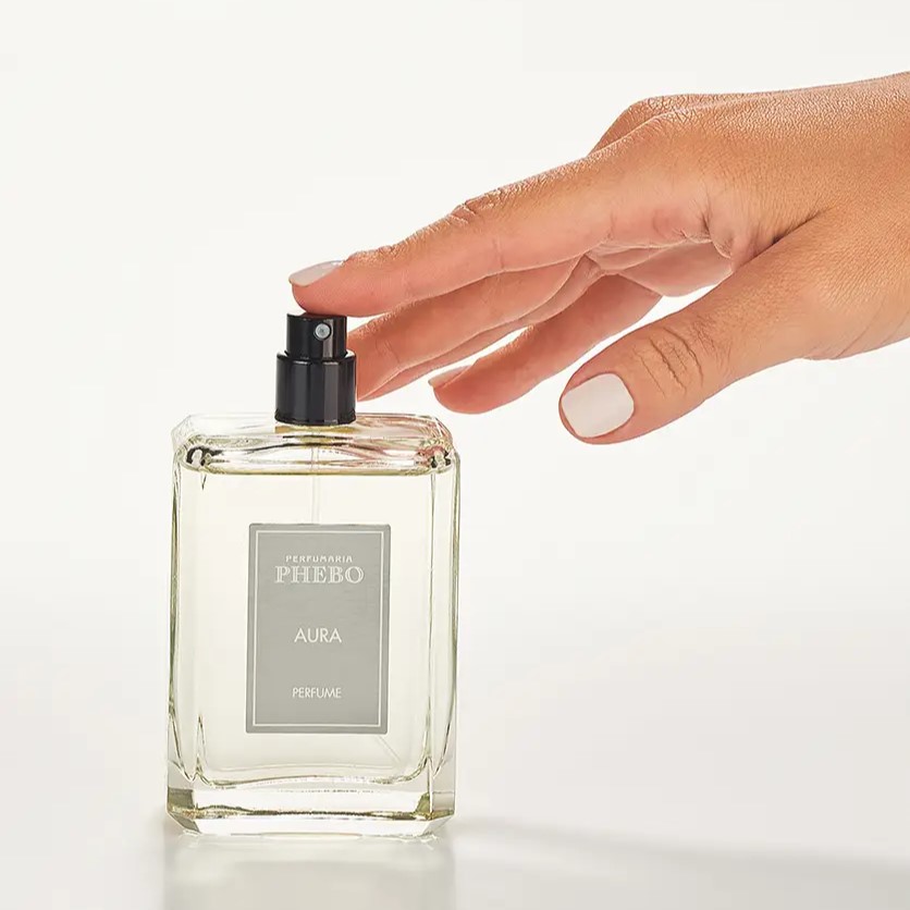 Mão feminina apertando o frasco do Perfume Aura da Phebo