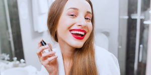 Mulher de cabelos compridos sorrindo para a câmera com um frasco de perfume na mão