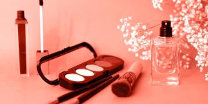 Itens de maquiagem e um frasco de perfume sobre uma superfície em tom de rosa claro