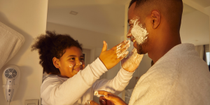 Homem negro brinca com sua filha, que espalha espuma de barbear em seu rosto