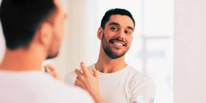 Homem sorridente passando perfume em frente ao espelho