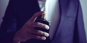 Homem de terno segurando um frasco de perfume escuro