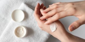 Close nas mãos de uma mulher passando creme em si mesma