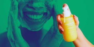 Close em mulher lavando o rosto ao fundo e uma mão feminina segurando um frasco do Limpador Facial Glicerinado Creamy à frente