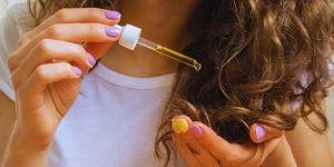 Close nas mão de uma mulher passando óleo em seus cabelos